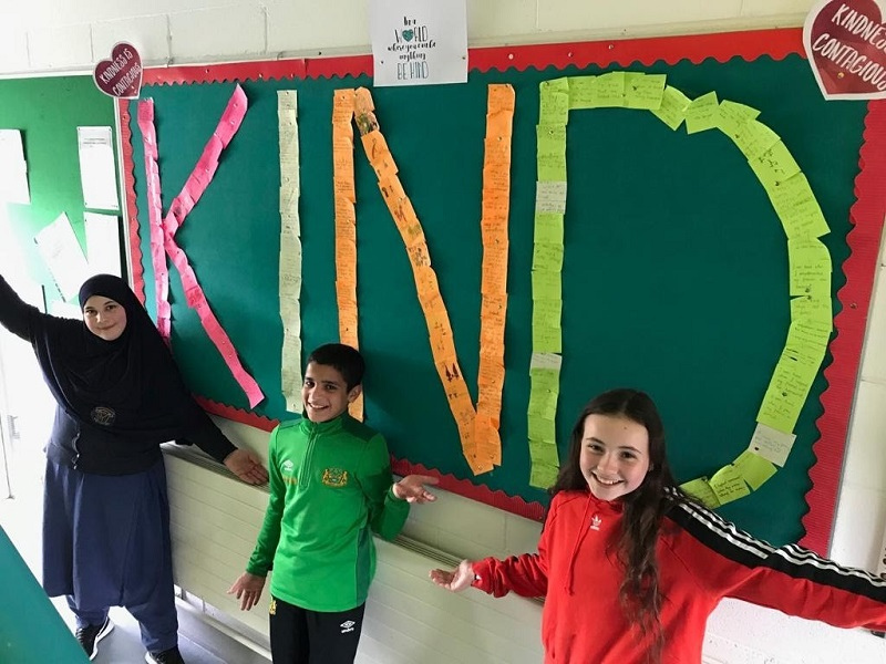 This is a photo of students from Scoil Treasa Naofa in front of a blackboard which has "Kind" spelt out in post-it notes.