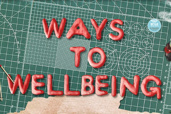 Still from a video of the Ways to Wellbeing exhibition showing the exhibition name in red font against a background of graph paper and school stationary