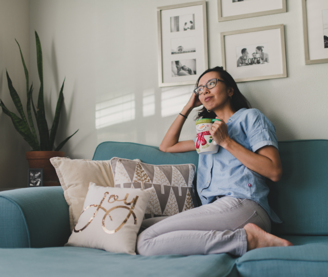 A mother takes some time for herself, relaxing on a sofa in a family room with a cup of tea.